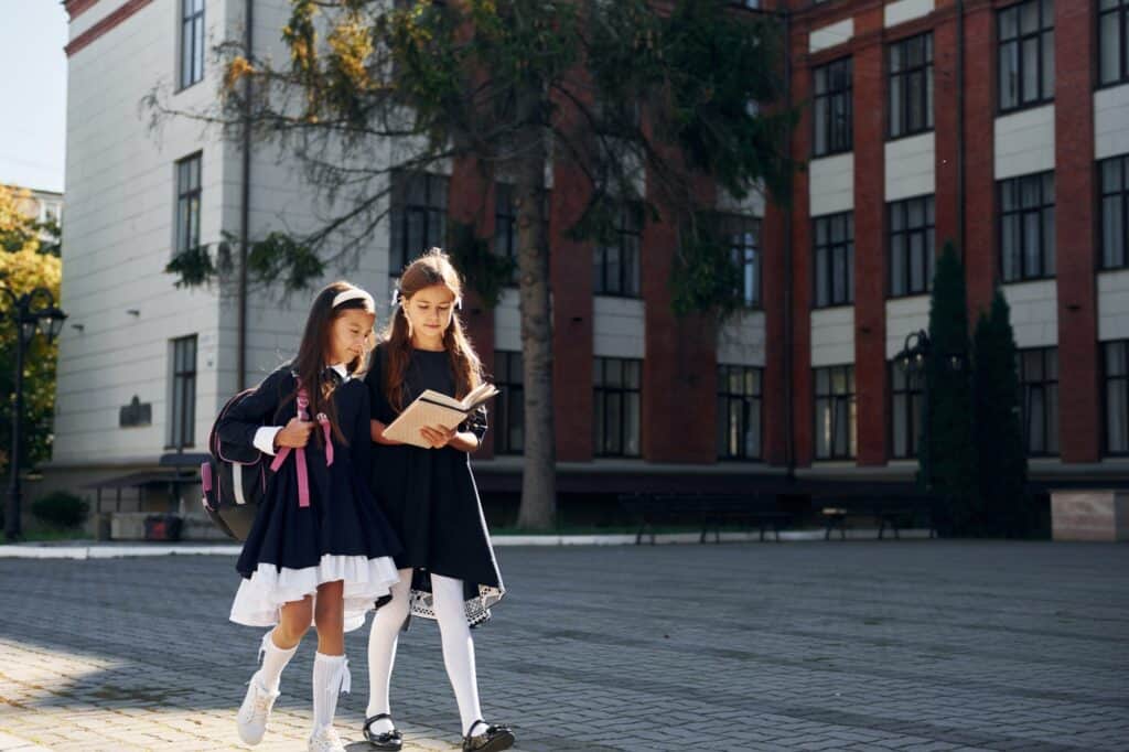 Two schoolgirls walking outside the school building in the concept of 'top schools in Wimbledon'.