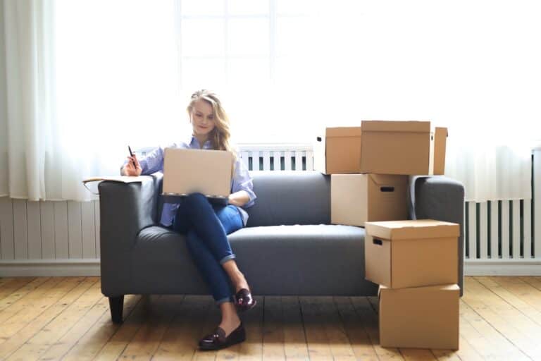 A young woman using her laptop while surrounded by moving boxes in the concept of 'What Are the Hidden Costs in Home Removals Services'.